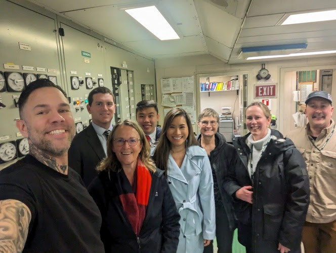 Eight people posing for a photo in a ferry engine room