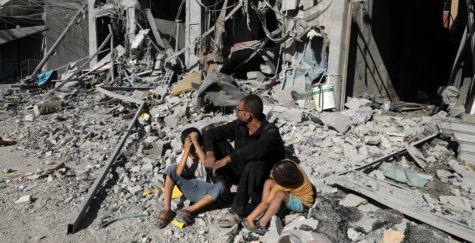 A man and two children sit amongst the rubble of destroyed buildings in Gaza.