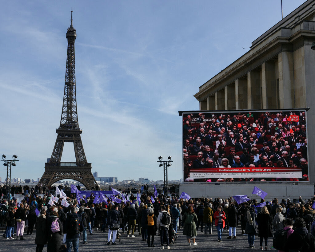 People with purple flags standing and watching a giant screen near the Eiffel Tower in Paris.