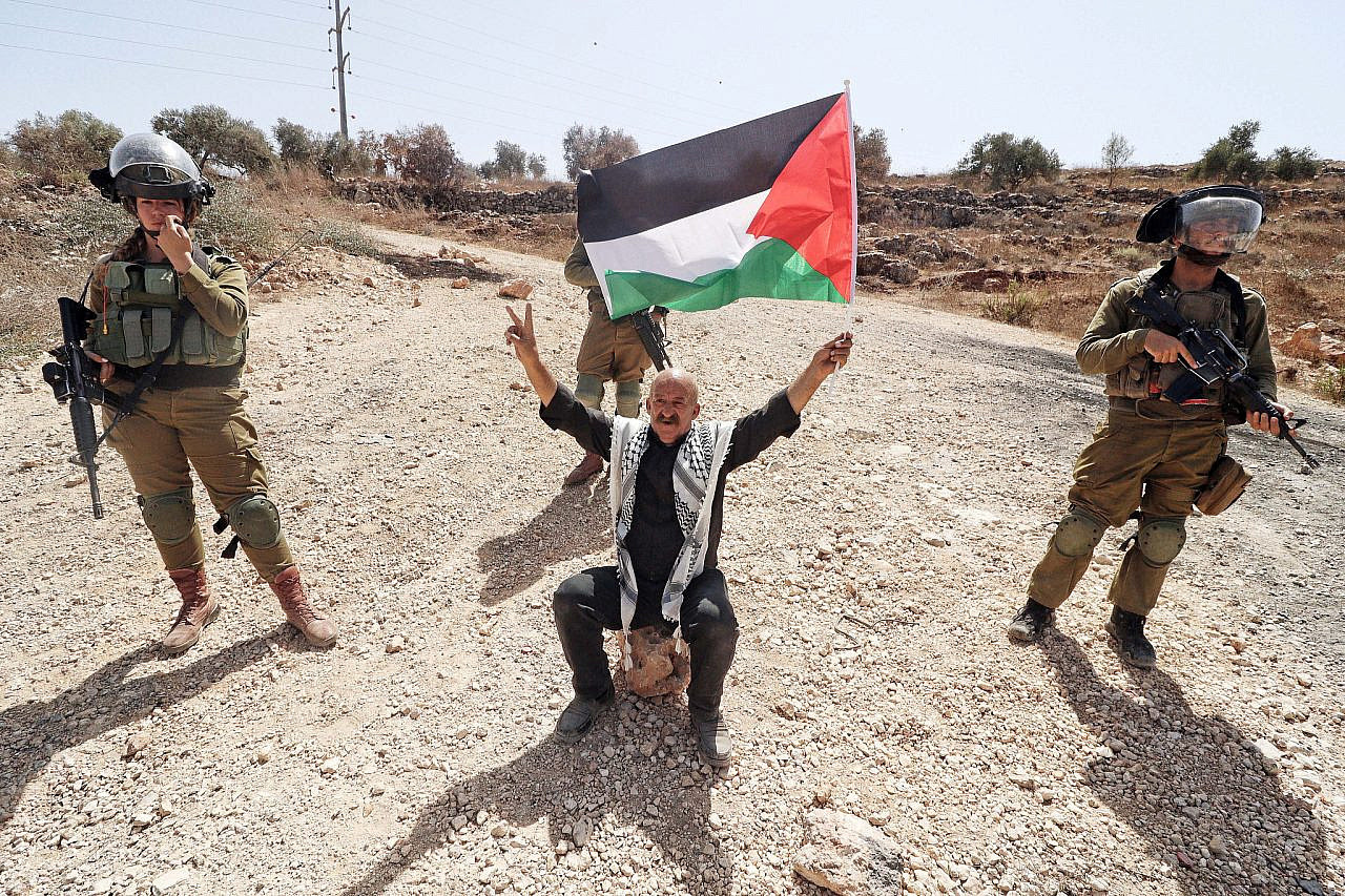 A protester raises the Palestinian flag in front of Israeli soldiers during a demonstration in Beita, occupied West Bank, September 8, 2023. (Wahaj Bani Moufleh/Activestills)