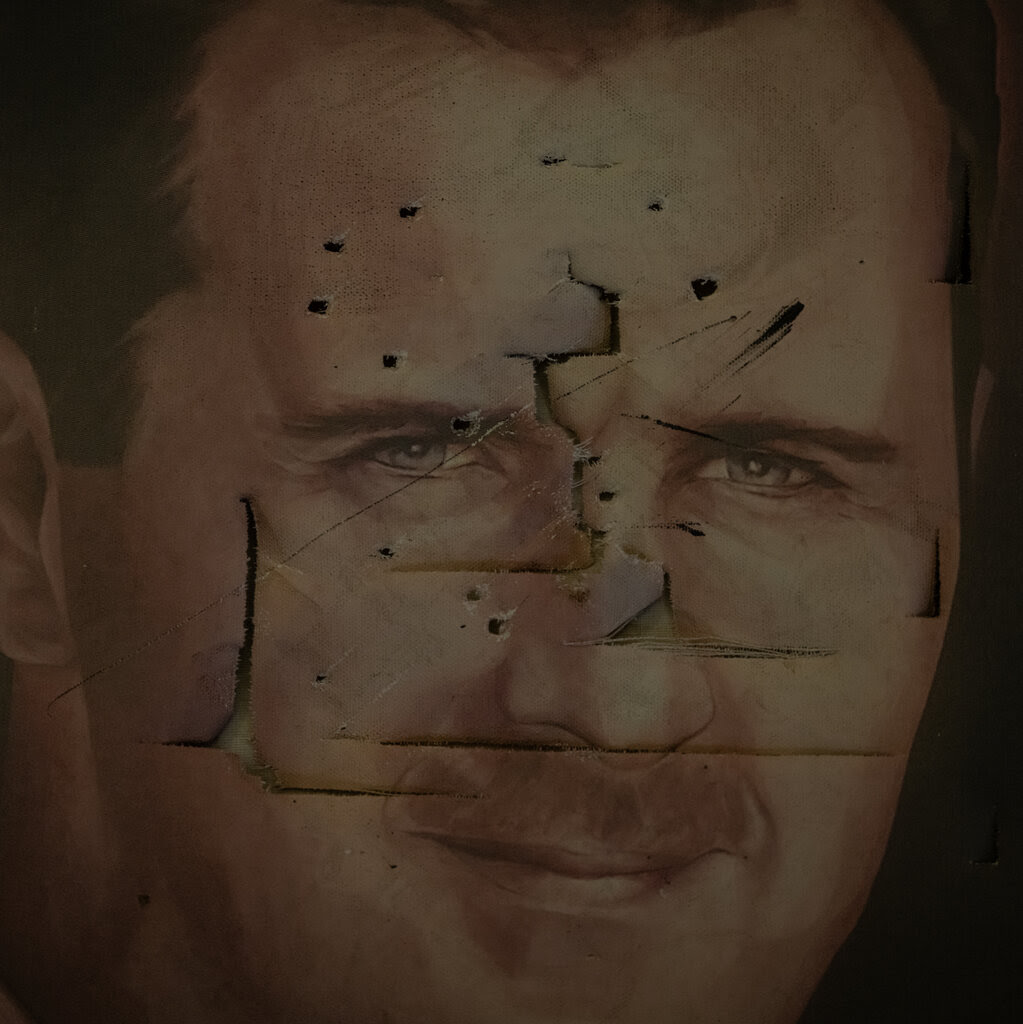 A portrait of a Bashar al-Assad, the deposed Syrian leader, looks like it has bullet holes and is ripped and defaced.