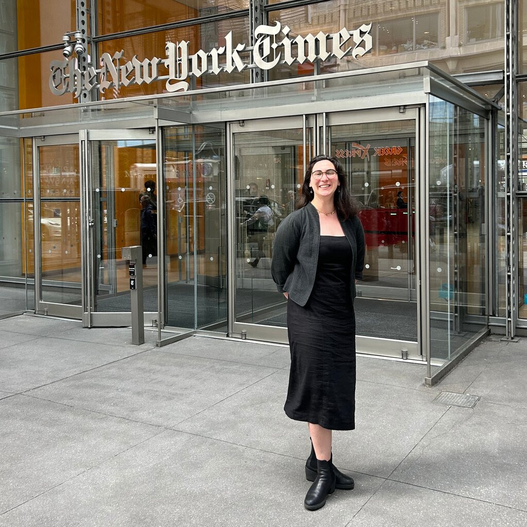 A woman in a black dress stands in front of The New York Times building. 