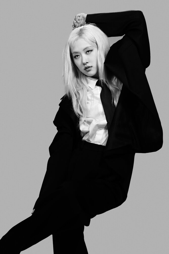 A black-and-white full-length portrait of Rosé, mid-dance move, in a pantsuit dark enough to appear like a silhouette.