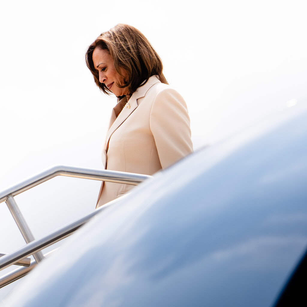 Kamala Harris, wearing a white jacket, walks down the steps leading out of a plane.