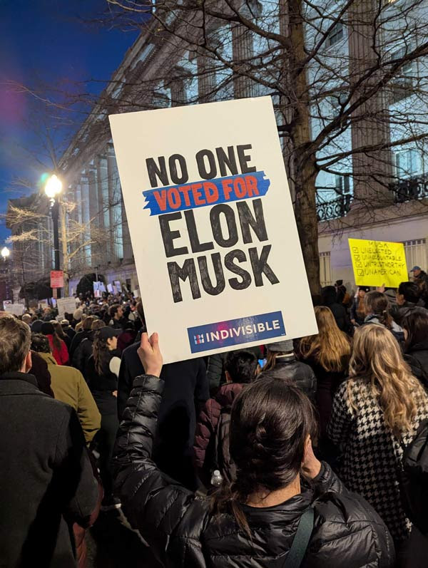 A protester in a crowd holding a sing that reads no one voted for Elon Musk