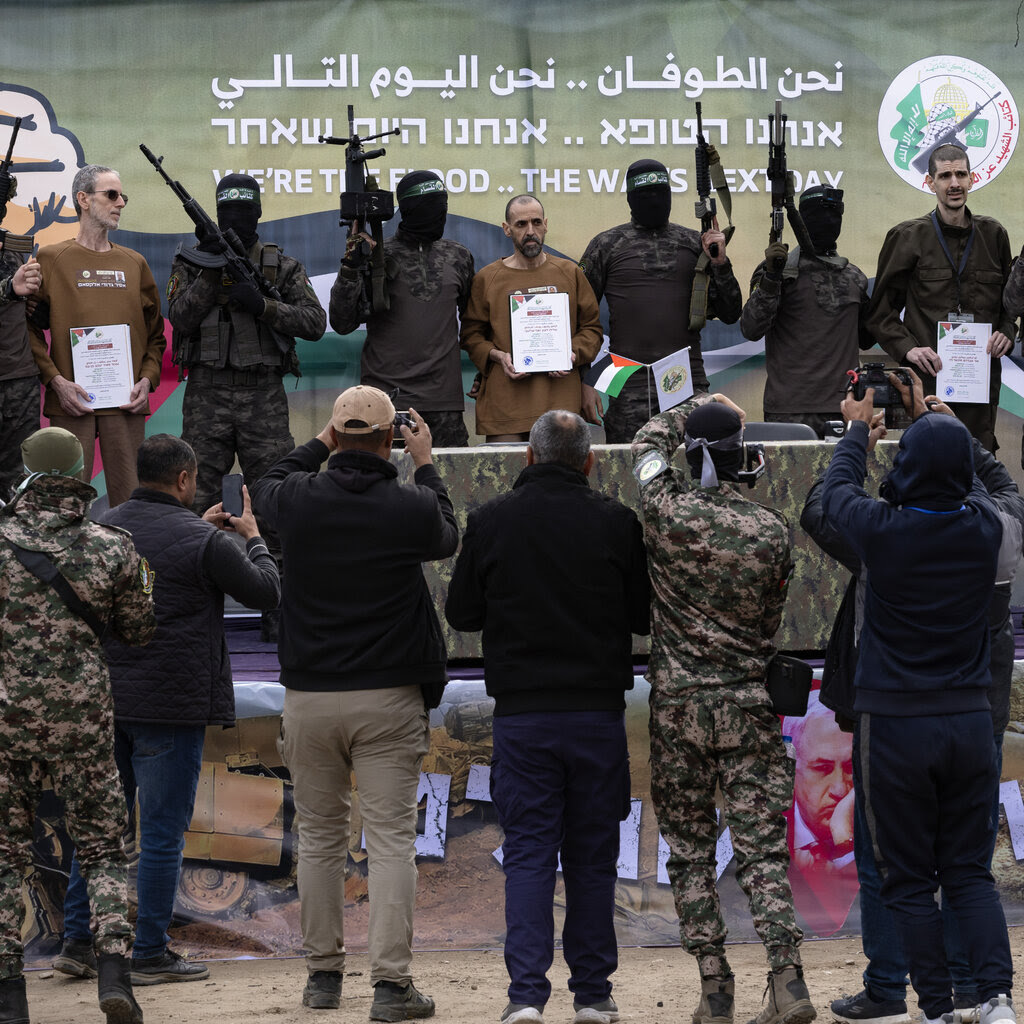 The three released Israeli hostages stand among armed and masked Hamas fighters as several people take their photo.