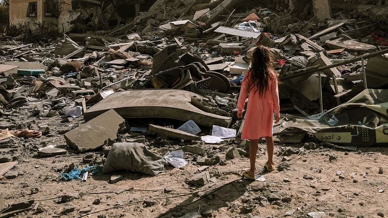 A child standing in a pile of rubble

Description automatically generated