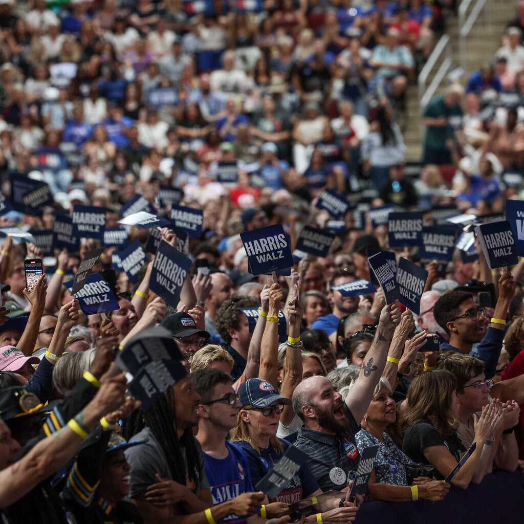 A crowd of people wave signs that say “Harris Walz” at a rally in Glendale, Ariz.