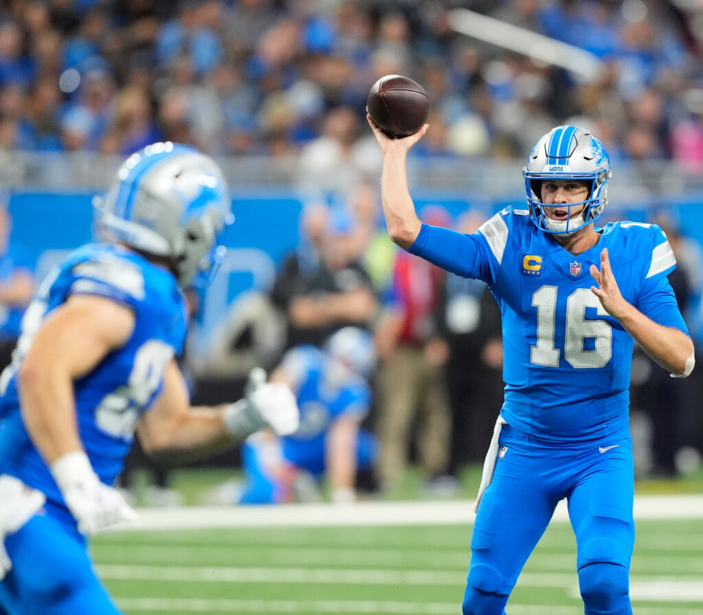 A Detroit Lions player throws the ball to a teammate, wearing a blue jersey and blue pants.