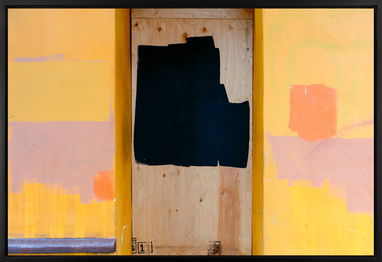 Color image of a large photograph of a yellow exterior wall with colorful paint splotches and wood covering its surface 