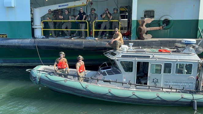 Several people in camouflaged clothing, some on a ferry and some on a rescue boat