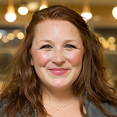 A head shot of Amy Rencher, a smiling woman with red hair and a rosy, pleasant complexion