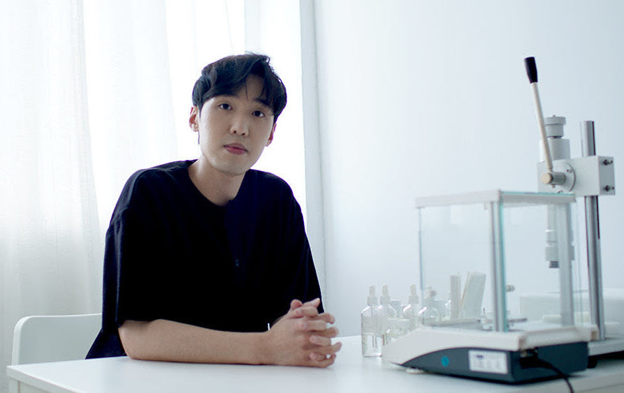 Perfumer Michael Wong sitting at a white desk with perfumery equipment.