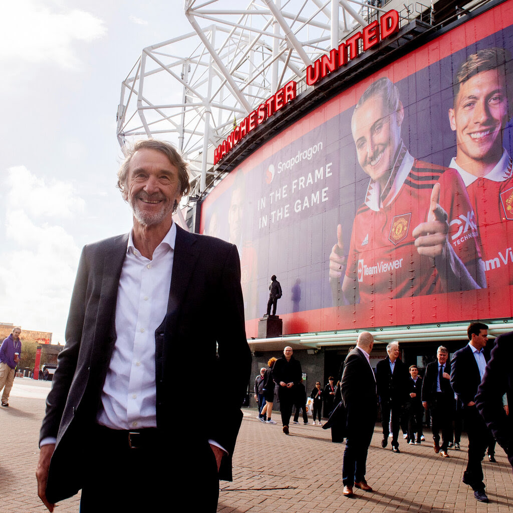Jim Ratcliffe stands outside Manchester United’s stadium as other people walk past.