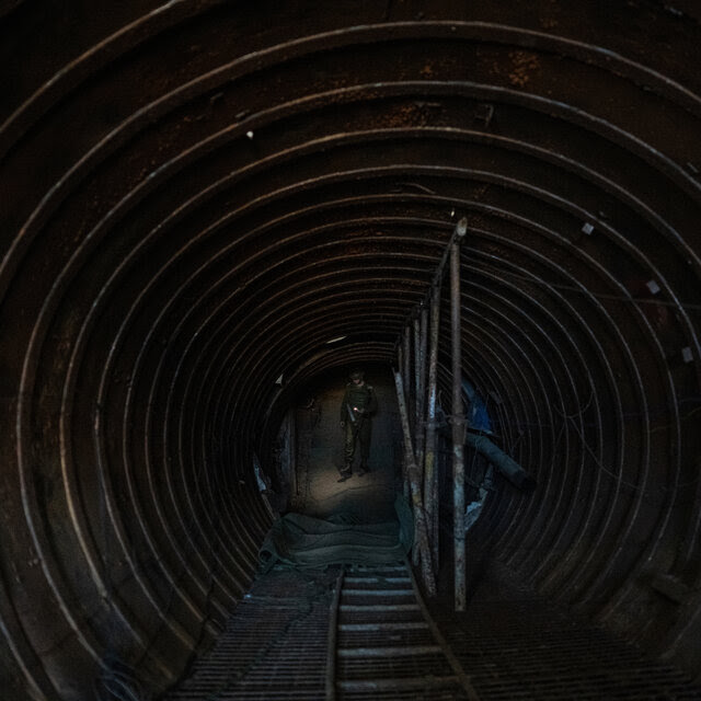 The interior of a large tunnel. A soldier is in the background holding a light.
