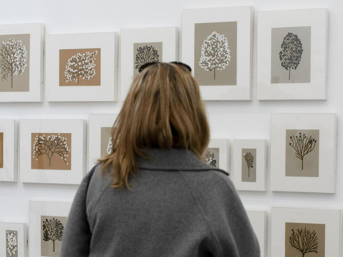 A woman stands in front of a collection of framed prints of trees
