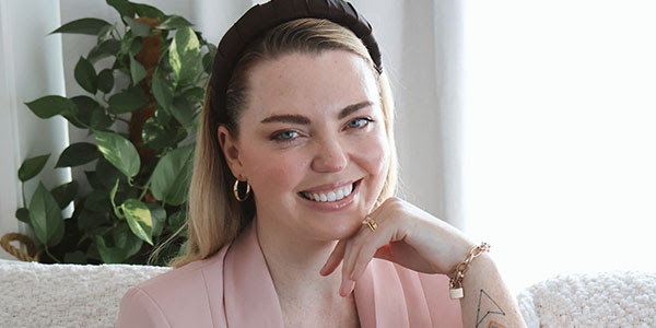 A person sitting on a couch with their head resting on their hand, looking at the camera and smiling