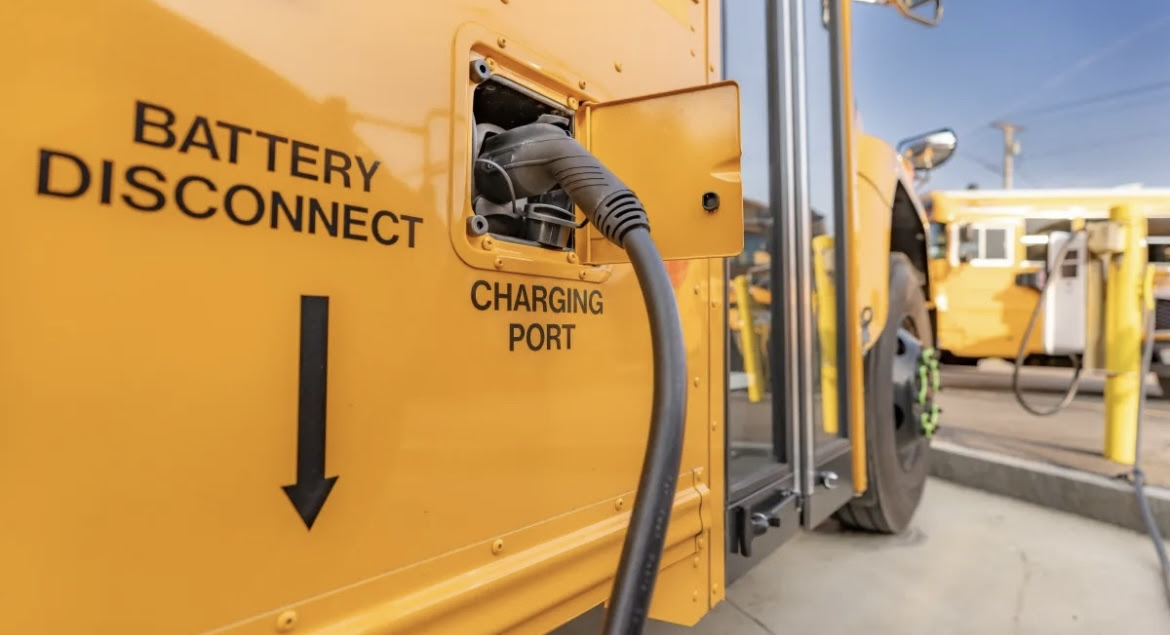 Picture of a large yellow school bus connected to a battery charging port. Picture credits to Getty Images