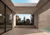 Mediante puertas giratorias de cristal se accede del salón a una terraza protegida por una pérgola de hormigón.