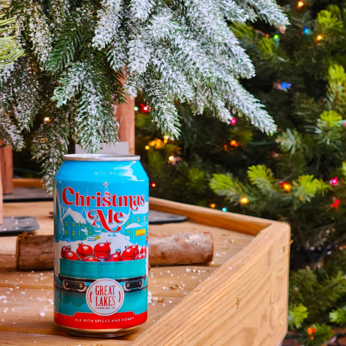 Can of Christmas Ale placed at the foot of an evergreen tree and beside a Christmas tree.