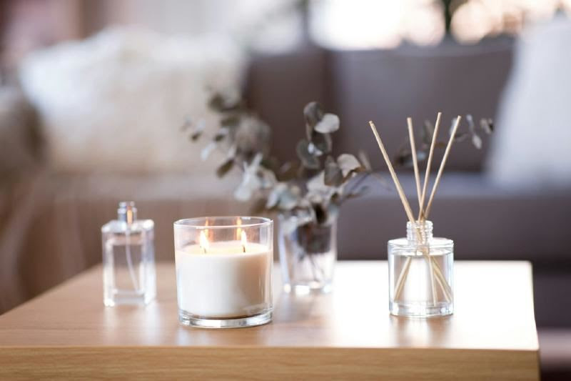 A candle and fragrance sticks on a table

Description automatically generated