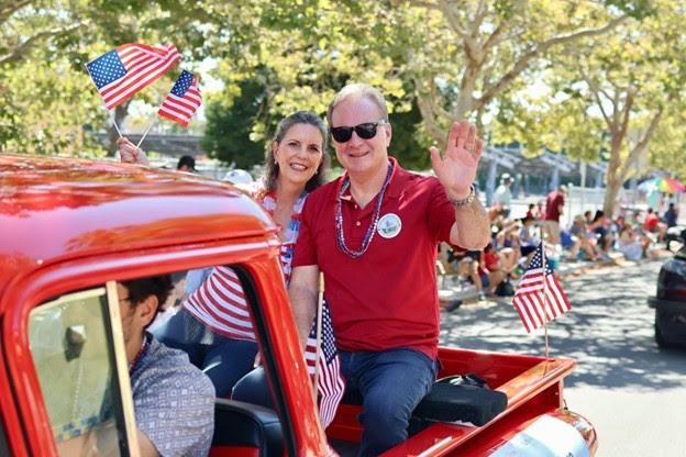 Dave and Pattie Cortese riding in the back of a bright red 1957 Chevy classic pickup truck.