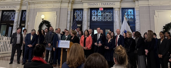 a crowd of people in businesswear stand behind
governor healey and lieutenant governor driscoll, who are behind a
podium facing the camera