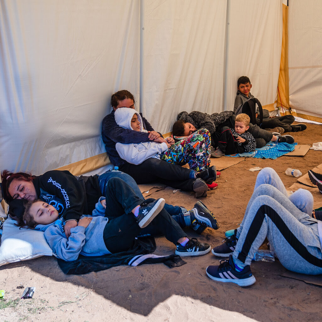 A group of adults and children lying or sitting on the ground inside a tent. 