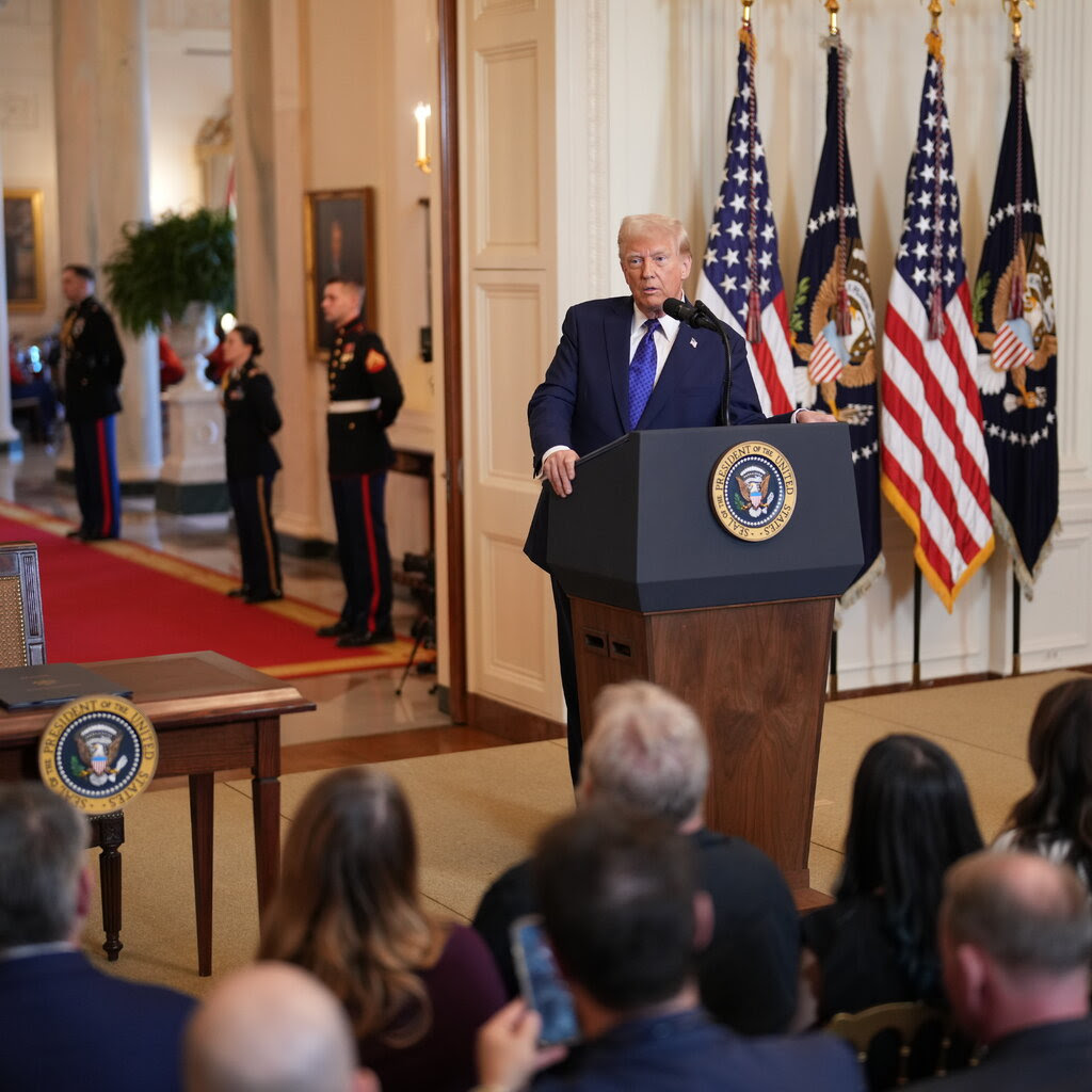 Donald Trump standing at a lectern in front of a row of seated reporters. 