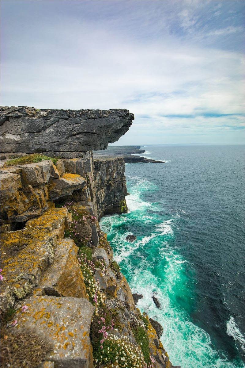 The high cliffs of the prehistoric hill fort of Dún Aonghusa on the Aran Island of Inishmore, Galway. Below, the sea is electric blue and foamy near the shore, while further out is a very dark blue.