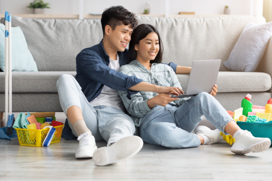 A young couple lean against a couch and read a laptop as they search for the best London, Ontario neighbourhoods in which to rent an apartment