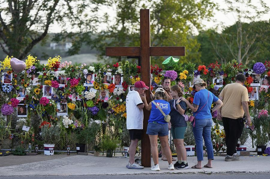 People gather at a memorial wall with flowers and photos of flood victims.