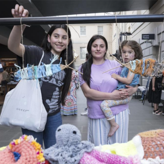 Woman with daughter in her arms and a teenager girl to the left in front of fabric toys
