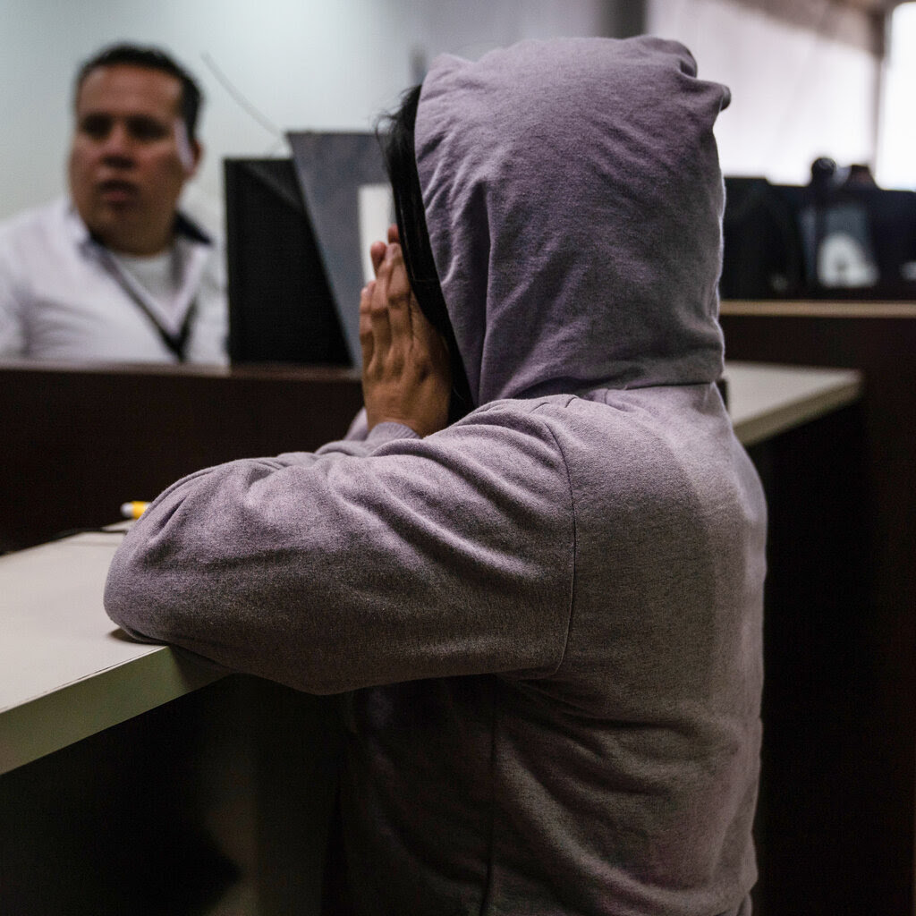 A migrant in a hoodie, covers her mouth, her elbows on a desk. 