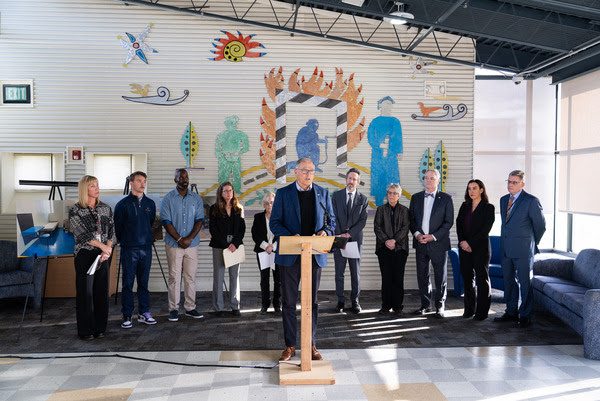 Gov. Jay Inslee speaks at a podium flanked by lawmakers, agency leaders, and stakeholders.