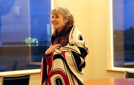 Patty Wood smiles while wrapped in a black, red, and white blanket with Native designs.