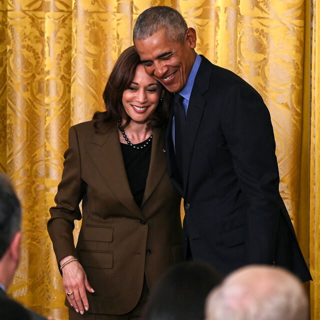 Barack Obama smiling and putting his arm around Kamala Harris, also smiling.