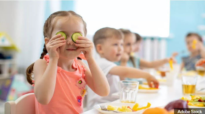Young children smiling and eating fresh fruits.