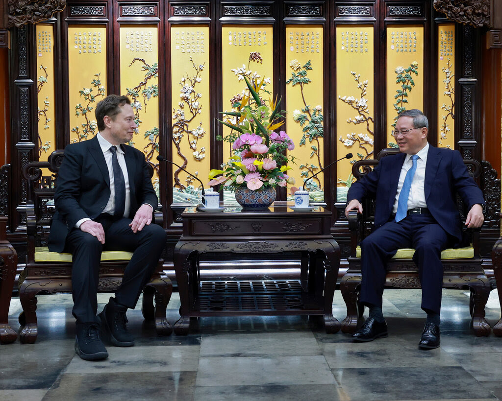 Elon Musk and Li Qiang, the Chinese premier, both wearing dark suits, white shirts and ties, sit alongside one another with a small table between them.