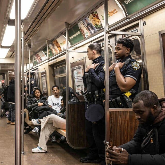 Police officers and passengers riding in a subway car.