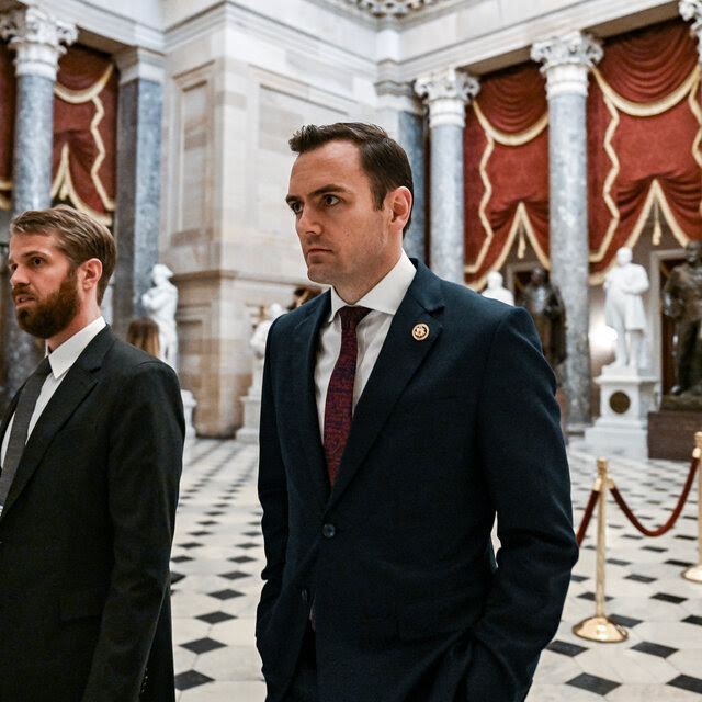 Representative Mike Gallagher, wearing a suit, walks with another man in the lobby of the Capitol.