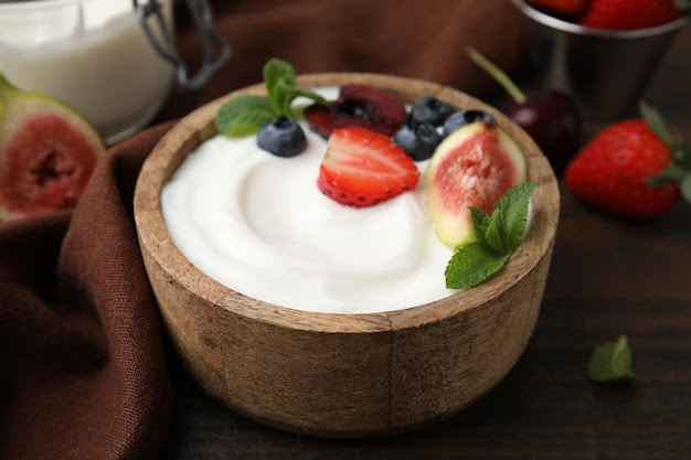 Un bol avec du yogourt, des baies, des fruits et de la menthe sur une table en bois.