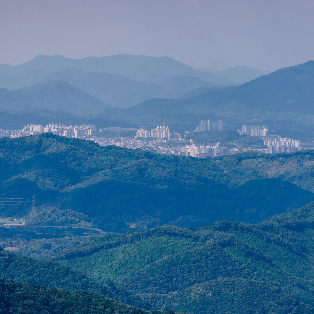 The skyline of a city is seen in the haze, surrounded by lush mountains.