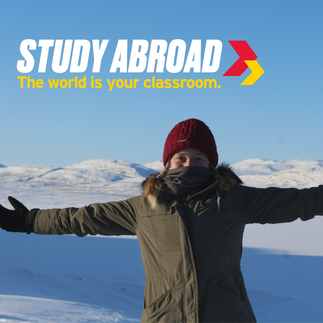 A student in a jacket, hat and a scarf that covers most of their face, holding their arms outstretched in front of a snowy scene. They look happy if a little cold. Text says "study abroad, the world is your classroom"
