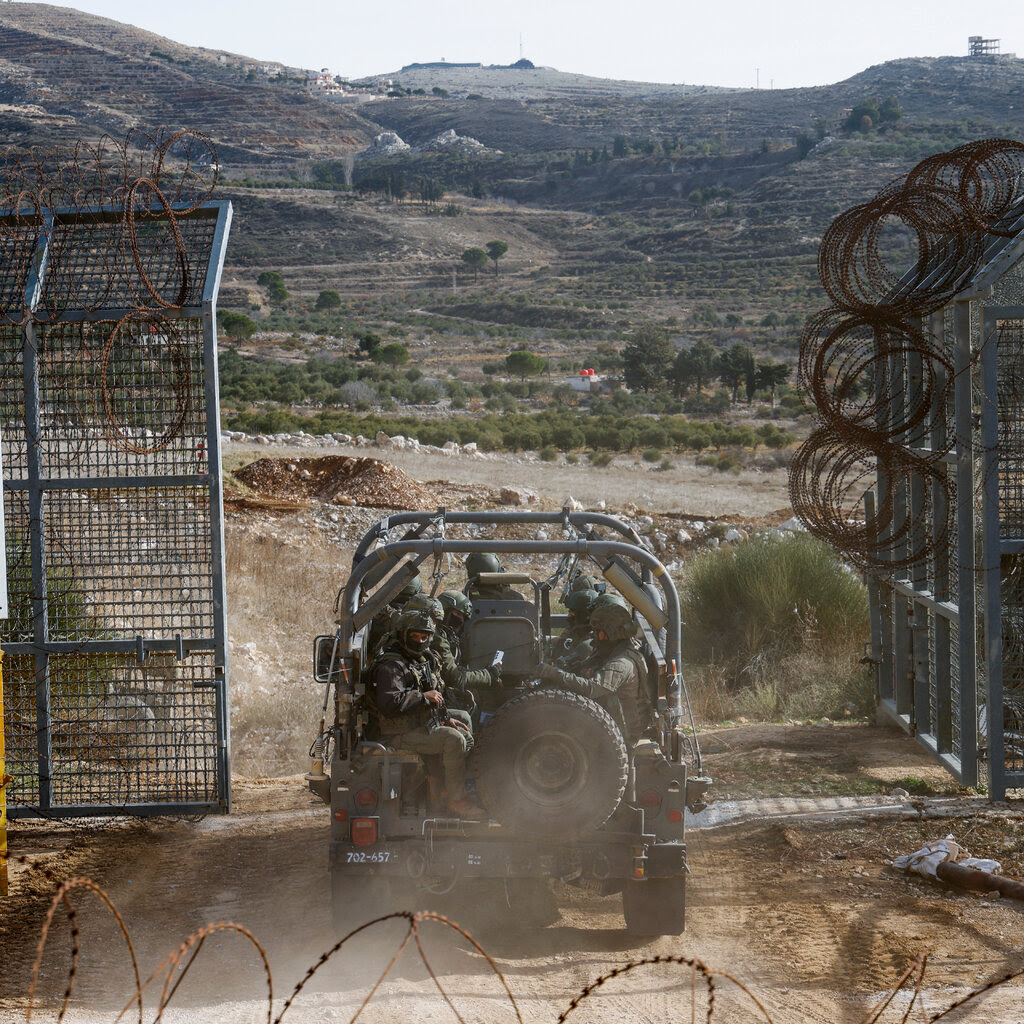 A military vehicle passes through the gate in a fence.