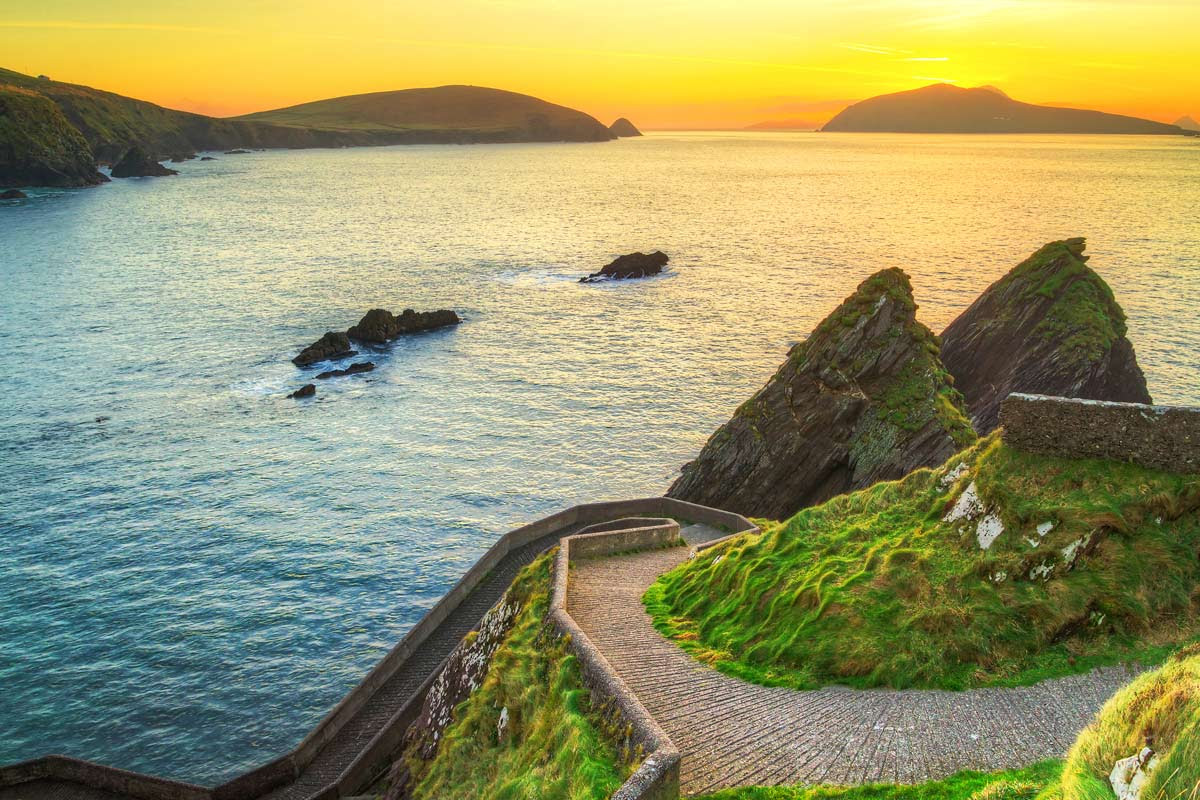 A photo of Corca Dhuibhne in Kerry, showing cliffside steps in the foreground, and sea, islands, and twilight in the background.