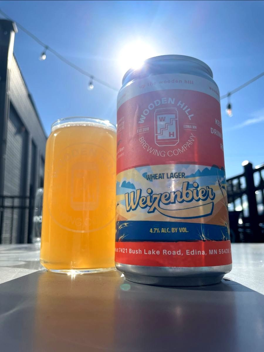 Image of a crowler can of "Weizenbier" Wheat lager next to a pint glass filled with a light, opaque beer. 