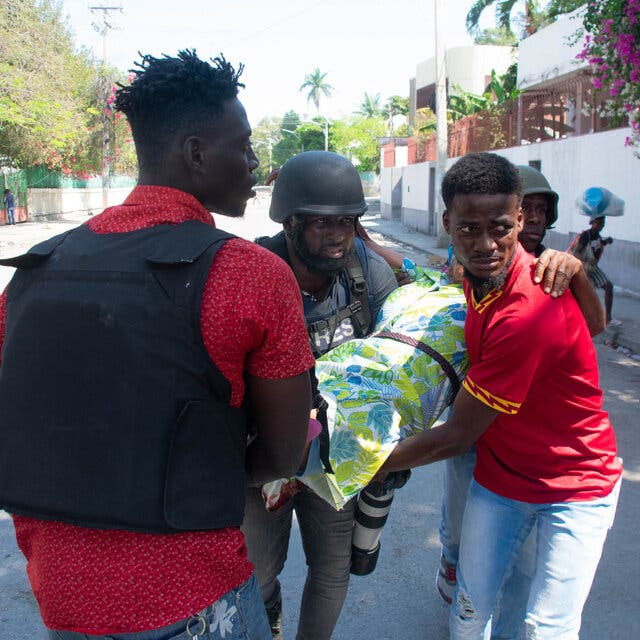 Three men carry a woman on a street.