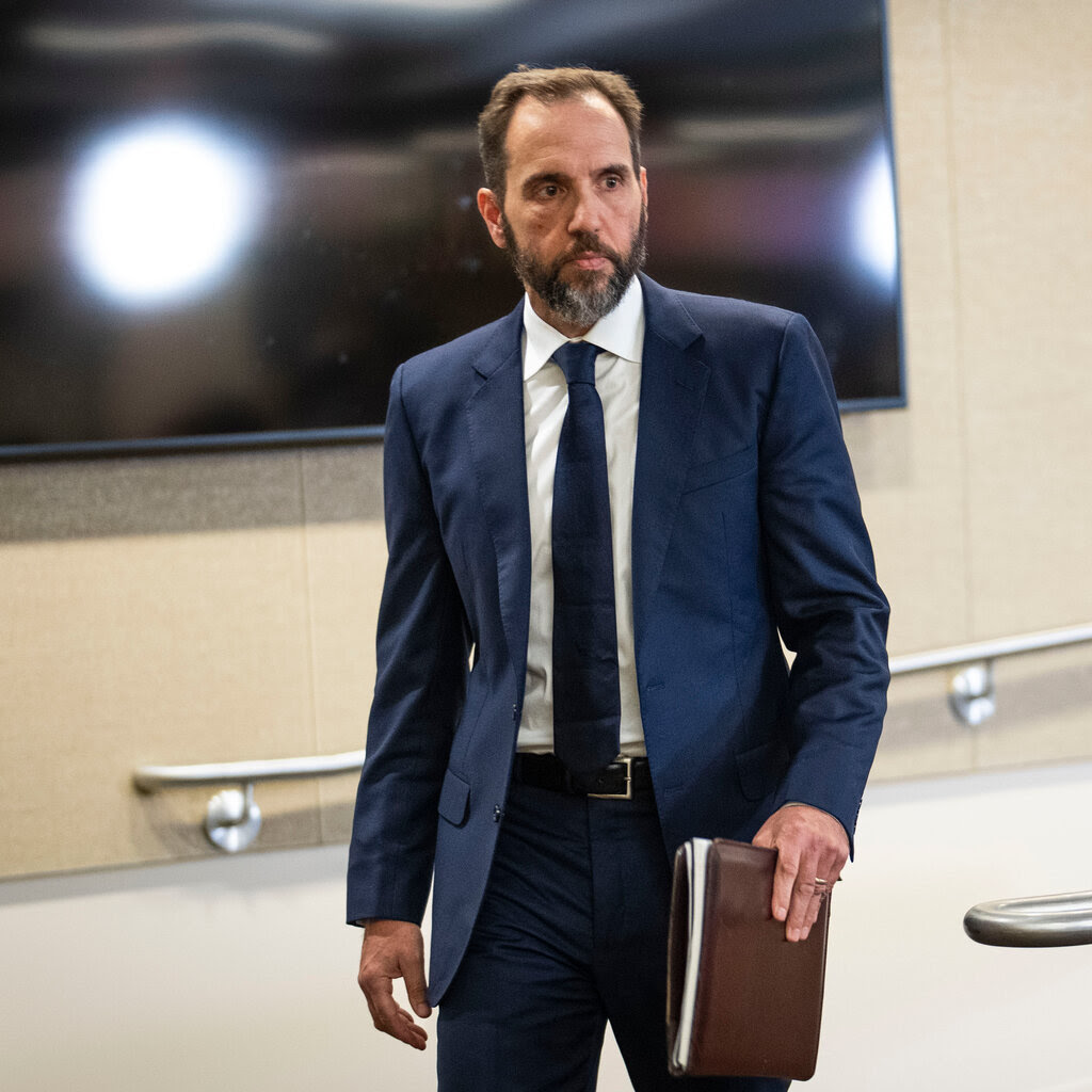 Jack Smith wearing a blue suit and carrying a portfolio in his left hand. 