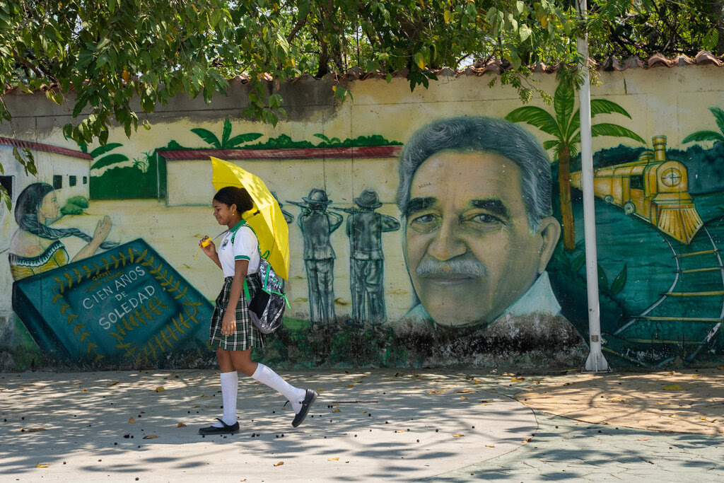 A girl walks with a yellow umbrella past a mural showing author Gabriel García Márquez.
